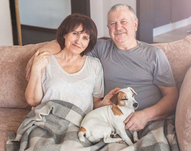 elderly couple sitting on the couch together with dog recovering from surgery in home care management geriatric care management