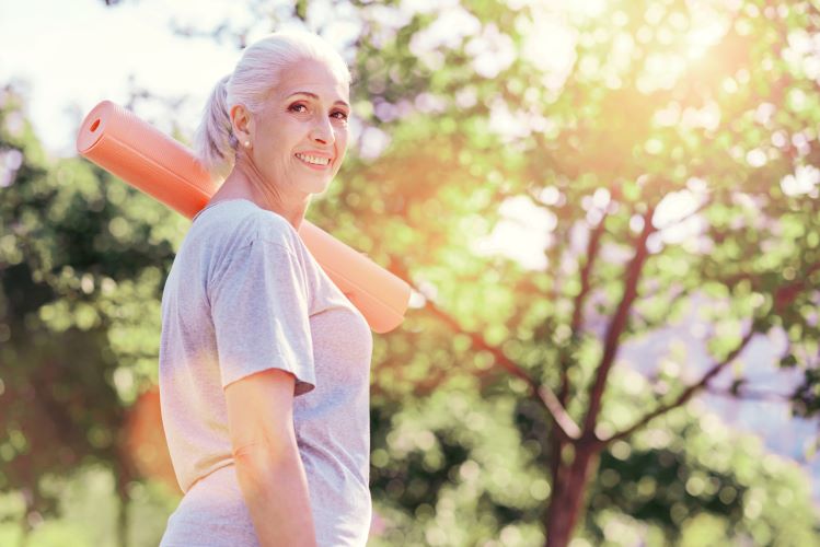 Older woman smiling while heading to yoga in the park